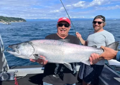 man proudly displaying his massive salmon catch alongside one of our guides